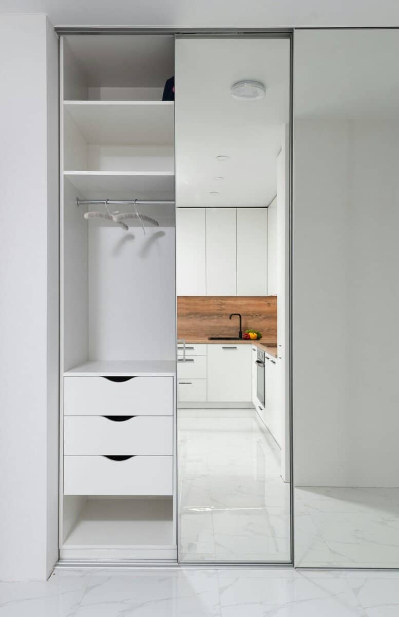 Modern white wardrobe with built-in shelves and mirrored sliding door, sleek storage solution.